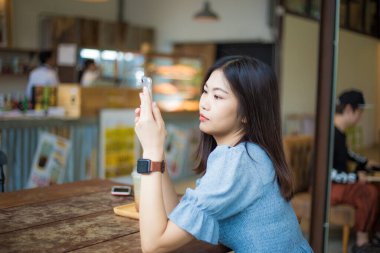 Kafede oturan Asyalı iş kadınları akıllı telefon iletişim sosyal camiası kullanıyor