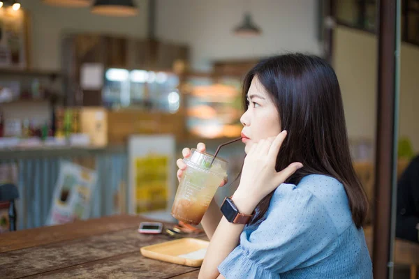 亚洲妇女坐在现代咖啡馆里喝冰块柠檬苏打水模糊了人们的背景 — 图库照片
