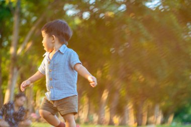 Küçük çocuk şehir parkında çimde koşuyor. Gün batımı zamanı. Ağaç dinlenme haftasonu.