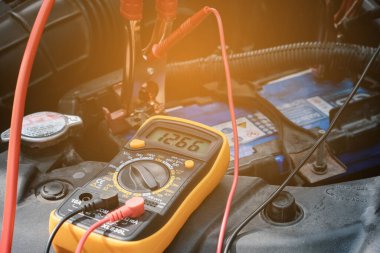 Tamirci el, bir araba aküsündeki voltaj seviyesini kontrol etmek için çoklu-metre voltmetre kullanır..