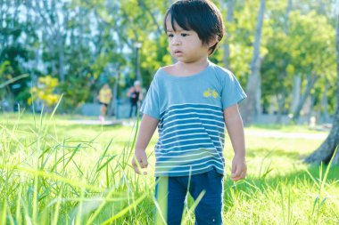 Doğada, parktaki yeşil çimlerde yürüyen sevimli Asyalı çocuk.