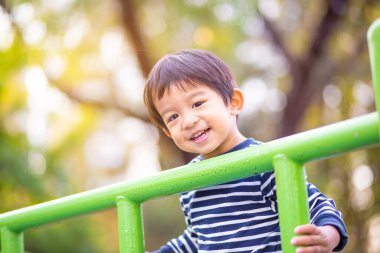 Mutlu Asyalı 2 yaşındaki çocuk şehir parkında çocuk parkında tırmanıp oynuyor.
