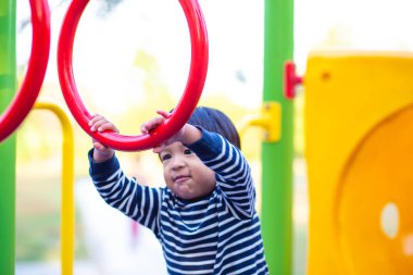 Mutlu Asyalı 2 yaşındaki çocuk şehir parkında çocuk parkında tırmanıp oynuyor.