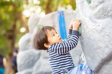 Mutlu Asyalı 2 yaşındaki çocuk şehir parkında çocuk parkında tırmanıp oynuyor.