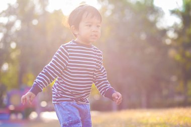 Parktaki yeşil çimlerde oynayan küçük çocuk. Doğadaki gündoğumu çocuğu.