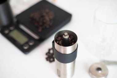 Beyaz arka planda, el tamircisi öğütücü kahve ve ölçülü ev içkisi ile sıcak kahve damlıyor.