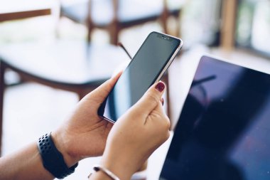 Kafede kahve içerken bilgisayarlı siyah cep telefonu kullanan bir kadının görüntüsü.