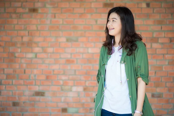 Junge asiatische Frau trägt grünen Kleiderständer vor Backsteinmauer b — Stockfoto