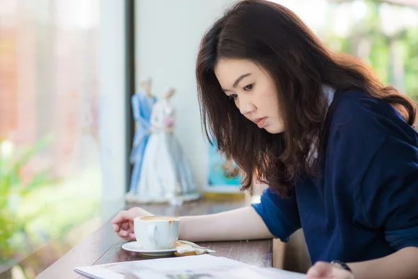 Азиатская студентка расслабляется с горячим кофе и журналом в кафе — стоковое фото