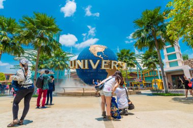 Tourists and theme park visitors taking pictures of the large rotating globe fountain in front of Universal Studios clipart