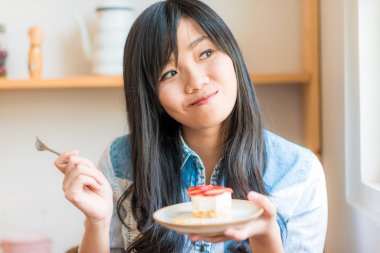 Genç Asyalı çok gülümseyen kadın café'de pasta yemeye portresi