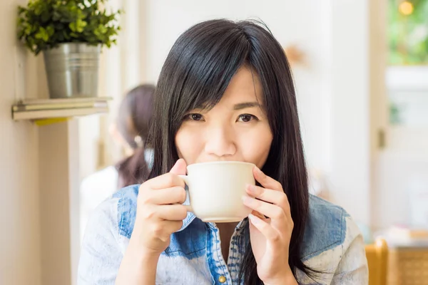Vrouw met kop koffie glimlachend in café — Stockfoto