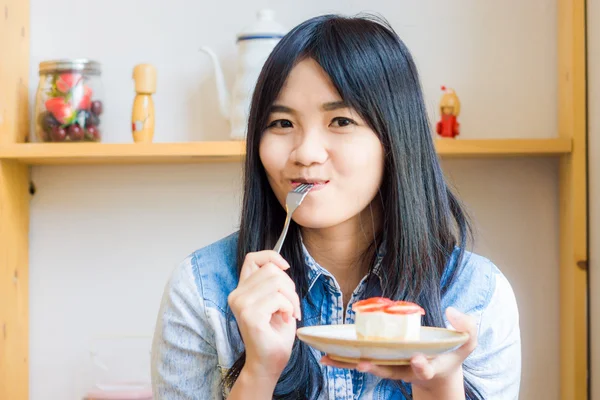 Asian smiling woman wearing jean shirt biting the piece of tasty