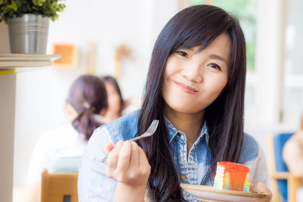 Asian smiling woman wearing jean shirt biting the piece of tasty — Stock Photo, Image