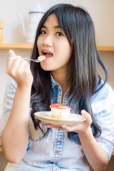 Kaunis hymyilevä nuori nainen puree mansikkakakkua leipomossa s — kuvapankkivalokuva
