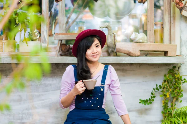 Όμορφη ασιατικές νεαρή γυναίκα με το φλιτζάνι του καφέ που ψάχνει για τη φωτογραφική μηχανή στο — Φωτογραφία Αρχείου