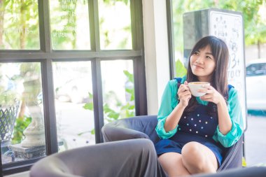 Mutlu Asyalı genç kadın kahve içiyor.