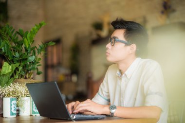 Kafede kahve içme ve dizüstü compute kullanan genç Asyalı adam