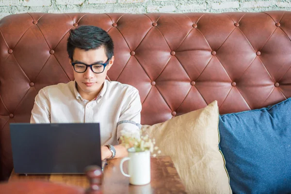 Young asian man drinking coffee in cafe and using laptop compute