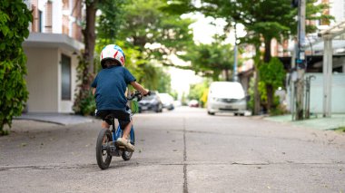 Asyalı okul çocuğu şehir merkezindeki köyde bisiklet sürmekten zevk alıyor.