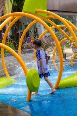 Küçük Asyalı anaokulu çocuğu yaz etkinliklerindeki açık su parkında eğleniyor.