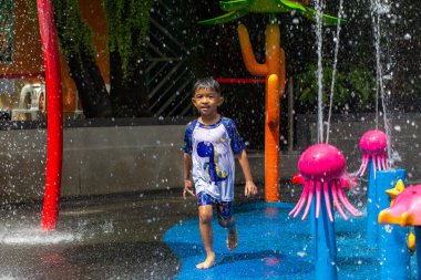 Küçük Asyalı anaokulu çocuğu yaz etkinliklerindeki açık su parkında eğleniyor.