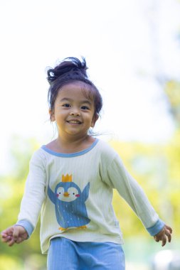 Yeşil çayırlarda koşan küçük Asyalı kız şehir parkındaki kızın keyfini çıkarıyor.