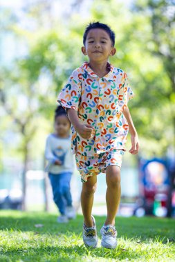 Anaokulu çocuğu şehir parkındaki açık alanda yeşil çimlerde koşmaya bayılıyor.