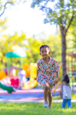 Anaokulu çocuğu şehir parkındaki açık alanda yeşil çimlerde koşmaya bayılıyor.
