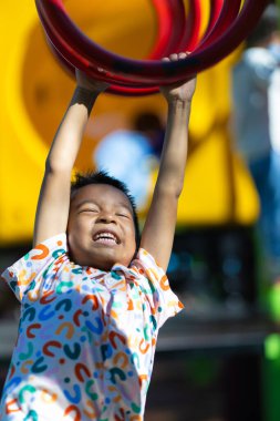 Küçük anaokulu çocuğu oyun parkına tırmanıyor, bar egzersizi yapıyor, parkın tadını çıkarıyor.