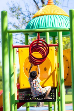 Küçük anaokulu çocuğu oyun parkına tırmanıyor, bar egzersizi yapıyor, parkın tadını çıkarıyor.