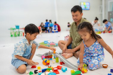 Baba sevimli anaokulu çocuğu ve kız çocuğuyla renkli oyuncak bloğu binasında oynuyor.