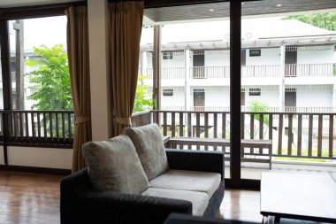 Otel odasında, perde ve halı döşeli modern gri renkli kanepe. Toprak tonlu tropikal otel tesisinde dekore edilmiş.