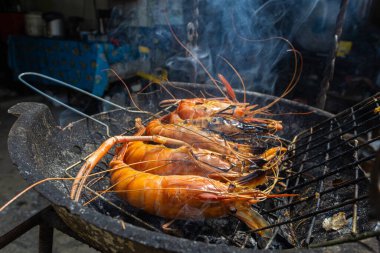 Nehir karidesi ev yapımı dumanlı deniz ürünleri ile ateşte kızartılıyor.