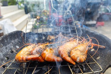 Nehir karidesi ev yapımı dumanlı deniz ürünleri ile ateşte kızartılıyor.