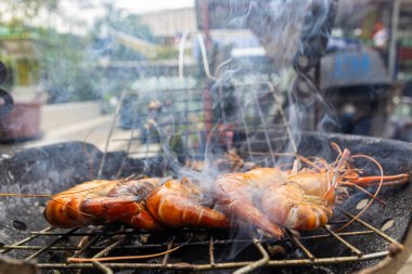Nehir karidesi ev yapımı dumanlı deniz ürünleri ile ateşte kızartılıyor.