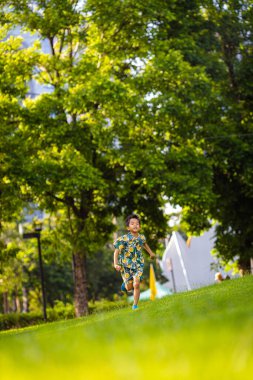 Asyalı çocuk yeşil çayırlarda koşmaktan zevk alıyor.