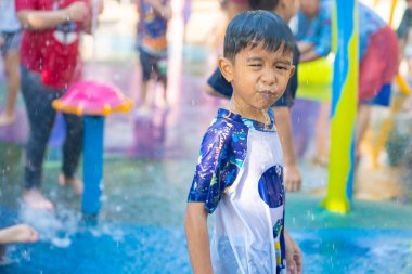 Küçük Asyalı 6 yaşındaki çocuk yazın açık havada su parkının suyuna su sıçratarak eğleniyor.