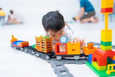 Küçük Asyalı anaokulu çocuğu beyaz oda eğitimi üzerine oyuncak tren bloğunun keyfini çıkarıyor ve öğreniyor.