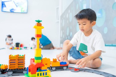 Küçük Asyalı anaokulu çocuğu beyaz oda eğitimi üzerine oyuncak tren bloğunun keyfini çıkarıyor ve öğreniyor.