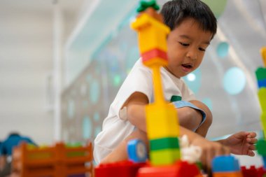 Küçük Asyalı anaokulu çocuğu beyaz oda eğitimi üzerine oyuncak tren bloğunun keyfini çıkarıyor ve öğreniyor.