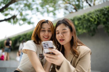 Mutlu Asyalı meslektaşlar iş günü dışarıda ofis binasında sosyal medya içeriğini araştırırken 5G kablosuz, komik kadın ortaklar internet bağlantısı kurarken hücresel uygulamayı tartışıyorlar.