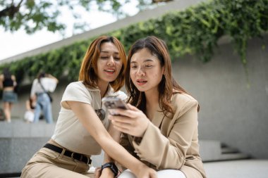 Mutlu Asyalı meslektaşlar iş günü dışarıda ofis binasında sosyal medya içeriğini araştırırken 5G kablosuz, komik kadın ortaklar internet bağlantısı kurarken hücresel uygulamayı tartışıyorlar.