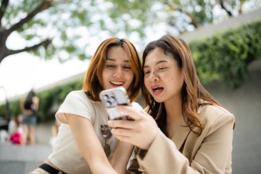 Mutlu Asyalı meslektaşlar iş günü dışarıda ofis binasında sosyal medya içeriğini araştırırken 5G kablosuz, komik kadın ortaklar internet bağlantısı kurarken hücresel uygulamayı tartışıyorlar.