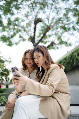 Mutlu Asyalı meslektaşlar iş günü dışarıda ofis binasında sosyal medya içeriğini araştırırken 5G kablosuz, komik kadın ortaklar internet bağlantısı kurarken hücresel uygulamayı tartışıyorlar.