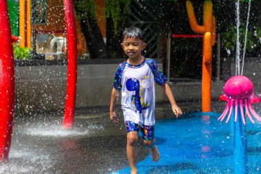 Küçük Asyalı anaokulu çocuğu. 6 yaşında. Yaz mevsiminde şehir merkezindeki su parkında eğleniyor.