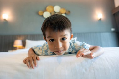 Küçük anaokulu çocuğu beyaz yastıklı otel odası seyahatinin tadını çıkarıyor.