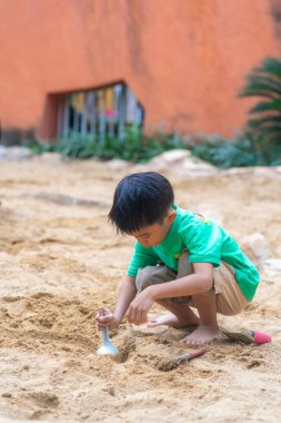 Sevimli küçük anaokulu çocuğu dışarıda kumlu çocuk parkında eğleniyor.