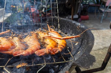 Dev nehir karidesleri ateşte kızartılıyor ve ev yapımı Asya deniz ürünleri pişiriliyor.