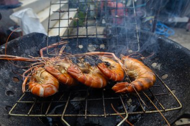 Dev nehir karidesleri ateşte kızartılıyor ve ev yapımı Asya deniz ürünleri pişiriliyor.